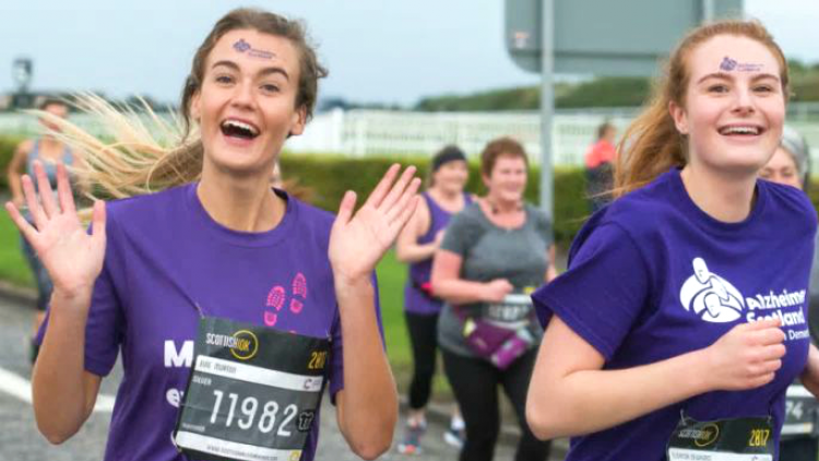 Two young women wave while running the Scottish 10k for Alzheimer Scotland