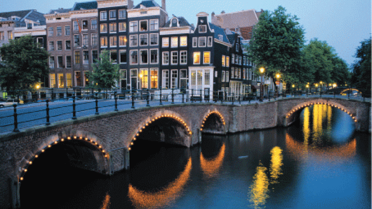 A canal in Amsterdam at night, light up with lights along the water