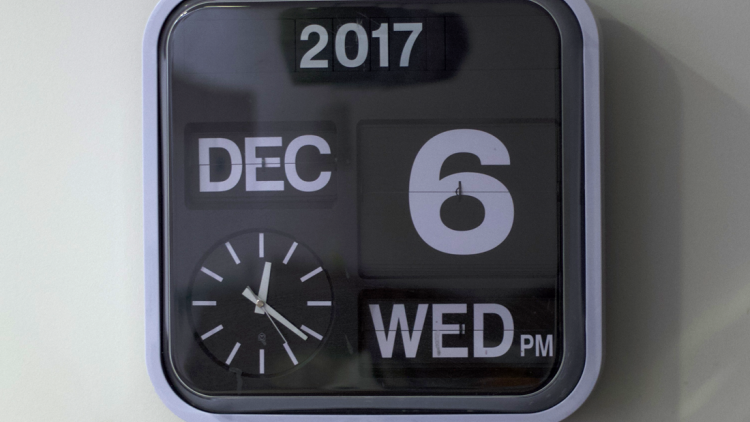A wall mounted black and white clock with the time, day and date in large scale