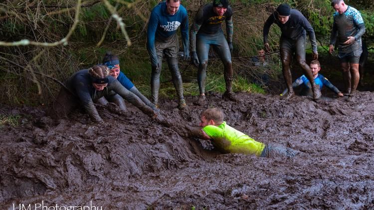 Image of a person stuck in mud with several people pulling them our using their arms