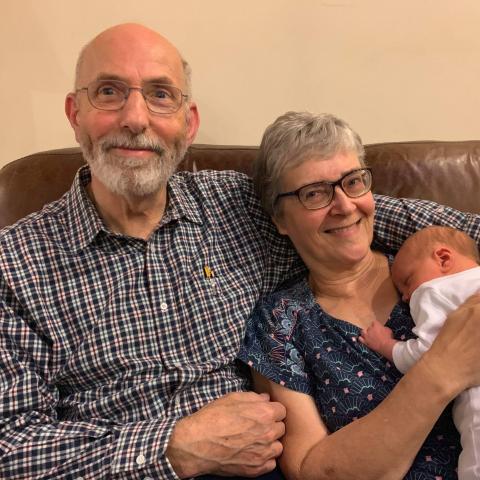 Morag and Ian are sitting on a sofa, holding a baby