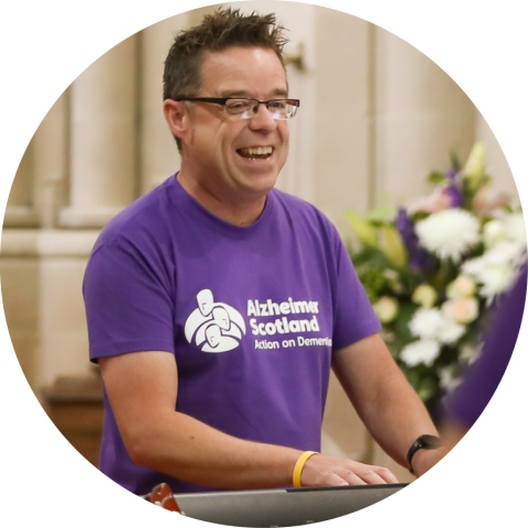 Bryan wears a purple t-shirt and smiles as he plays keyboard