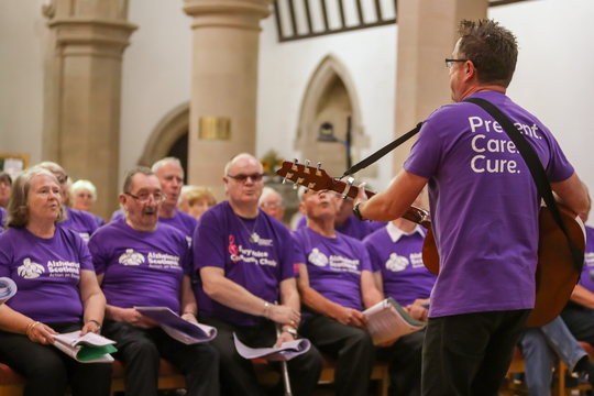 A man with a guitar leads an Alzheimer Scotland Choir Performance