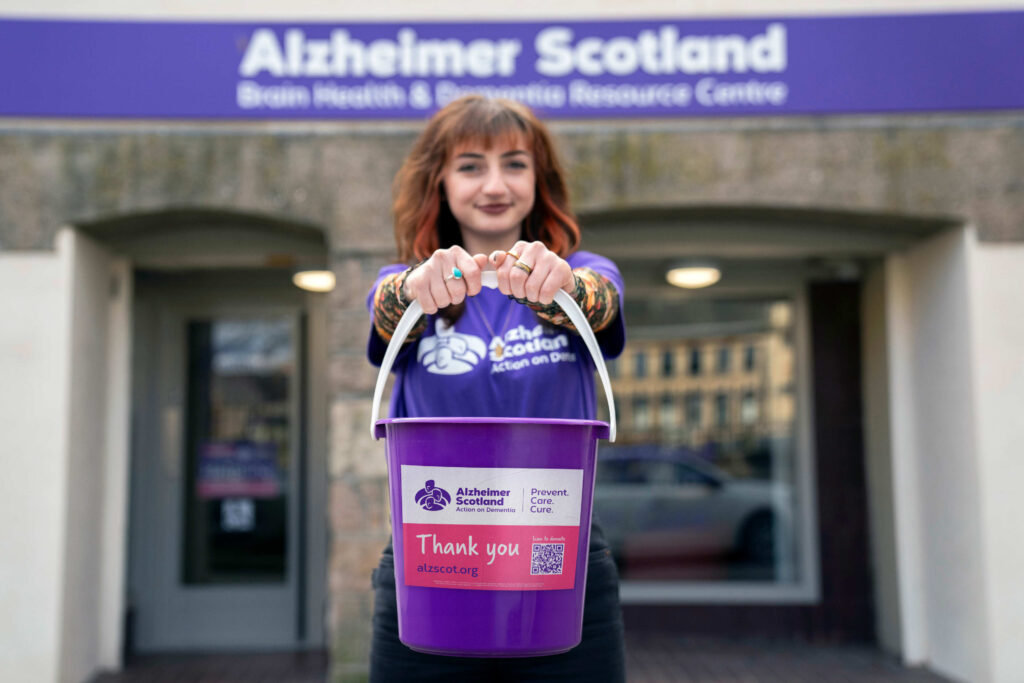 An Alzheimer Scotland member of staff collecting donations in a purple bucket