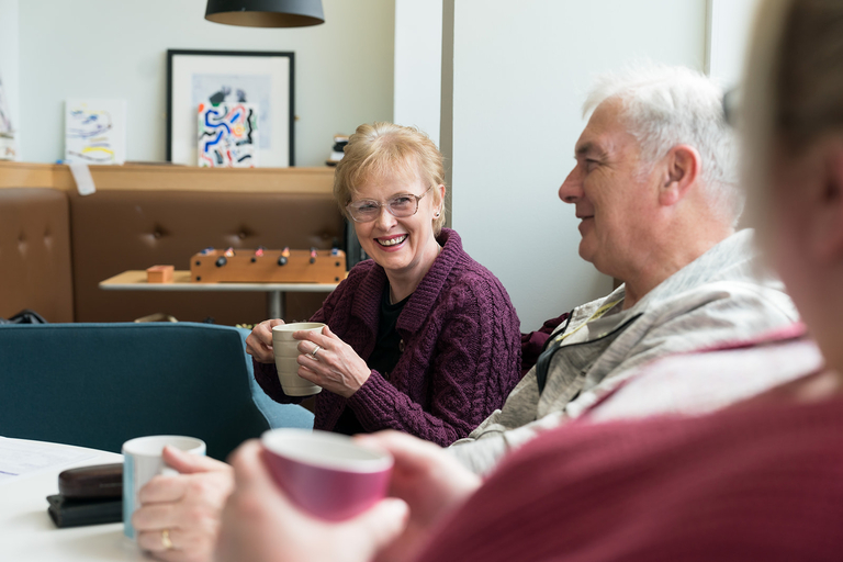 Woman in maroon cardigan enjoying cup of tea at Alzheimer Scotland group